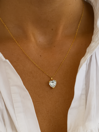 Gold necklace with a heart-shaped pendant on a person wearing a white top.