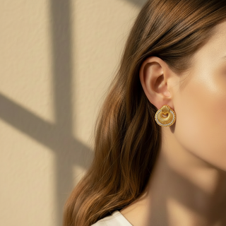 Close-up of a person wearing gold earrings against a beige wall.