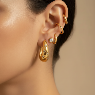 Close-up of an ear wearing gold hoop earrings with small stones on a neutral background