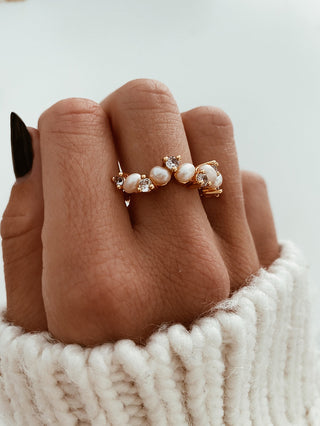 Freshwater Pearl Ring with pearls and cubic zirconia stones across a band ring in gold plating worn on a model with black pointed nails wearing a white knitted jumper from Zara - Gold Lunar