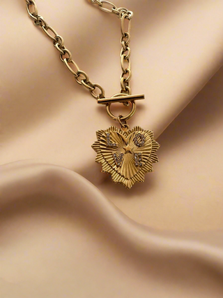 Gold necklace with a heart-shaped pendant on a beige fabric background