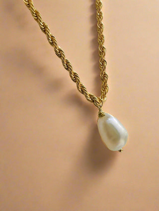 Gold chain necklace with a pearl pendant on a beige background