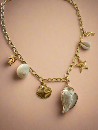 Gold chain bracelet with shell and star charms on a light background
