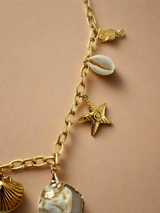 Gold chain bracelet with various charms on a light gray background