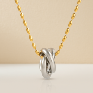 Silver knot pendant on a gold chain against a beige background