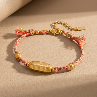 Bracelet with gold beads and pink thread on a beige background