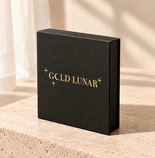 A black rectangular gift box with gold foil text reading 'GCLD LUNAR' and small star accents, standing on a beige stone surface in warm natural light.