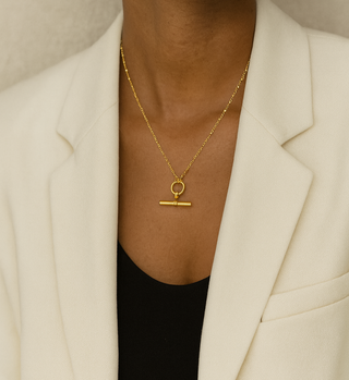 Person wearing a gold necklace with a minimalist pendant against a neutral background