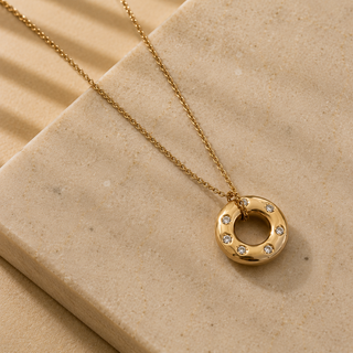 Gold necklace with a circular pendant on a beige stone surface