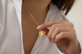 Gold Plated Opal Disc Necklace with the pendant being held by the model at the front. Model wears a white Zara shirt open at the front and has pointed pale pink gel nails.