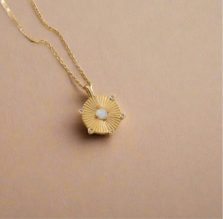 Gold Plated Opal Disc Necklace displayed on a mother of pearl dish from ZARA HOME with the light shining on the necklace creating shadows.
