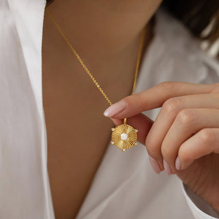 Gold Plated Opal Disc Necklace with the pendant being held by the model at the front. Model wears a white Zara shirt open at the front and has pointed pale pink gel nails.