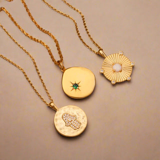 Gold Plated Opal Disc Necklace displayed in a velvet touch jewellery compartment drawer from Stackers. Displayed with two other necklaces, one gold hammered disc with a cubic zirconia embellished Hamsa Hand disc pendant and an another gold necklace, with an organic shaped disc with a green cubic zirconia star stone. All on fine gold trace chain.