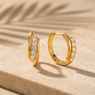 Gold hoop earrings with embedded stones on a beige surface