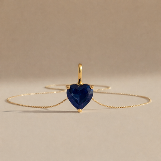 Gold bracelet with a heart-shaped blue gemstone on a beige background