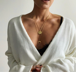 Person wearing a white cardigan with a gold necklace on a plain background