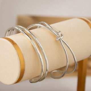 Silver Plated Knot Cuff Bracelet - Gold Lunar displayed on a cream and gold bangle bar with another silver plated hammered cuff bracelet.