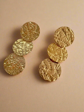 Triple hammered 18k gold plated disc drop earrings displayed on a white jewellery dish