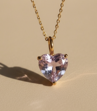Heart-shaped pink gemstone pendant on a gold chain against a beige background