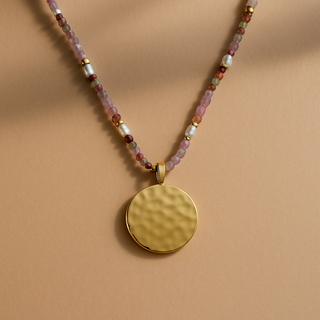 Necklace with a gold pendant and multicolored beads on a beige background