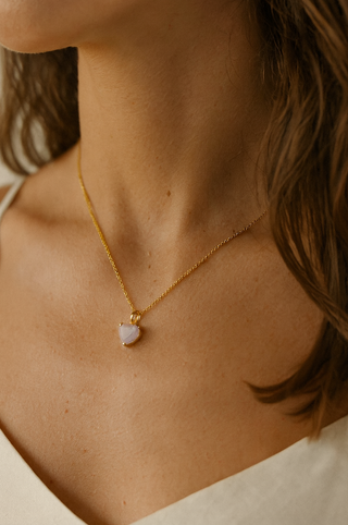 Close-up of a person wearing a gold necklace with a heart-shaped pendant.