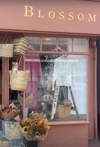 Storefront with 'Blossom' sign, displaying bags, clothing, and flowers.