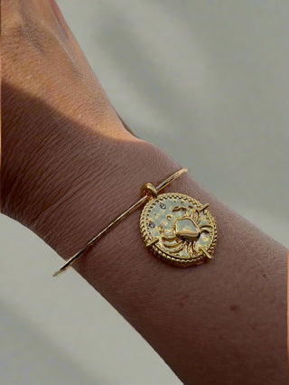 Gold bracelet with a detailed design on a wrist against a neutral background