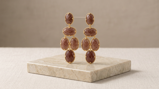 Gold earrings with brown gemstones on a beige marble stand against a beige background