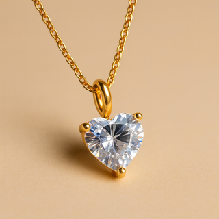 Heart-shaped crystal pendant on a gold chain against a beige background