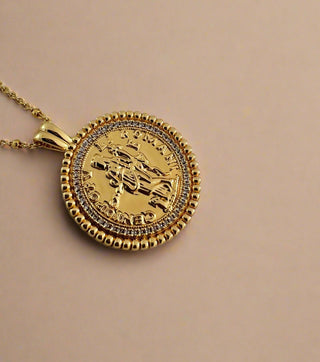 18k gold plated coin pendant necklace with cubic zirconia gemstones around the outside on a fine gold chain displayed on a pretty white porcelain jewellery dish