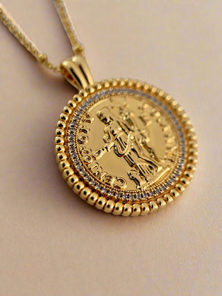 18k gold plated coin pendant necklace with cubic zirconia gemstones around the outside on a fine gold chain displayed on a pretty white jewellery dish close up