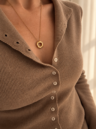 A close-up of a person wearing a gold ring pendant necklace over a brown ribbed knit button-front top.