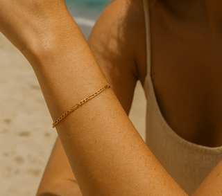 Close-up of a person's arm with a gold bracelet on a beach.