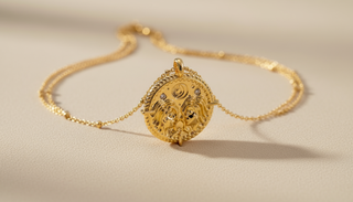 Gold necklace with an ornate pendant on a beige background