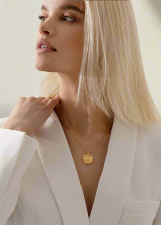 Woman wearing a gold necklace with a white blazer against a neutral background