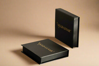 gold lunar jewellery branded black box with gold font. one box laid flat and one standing up in the sunlight.