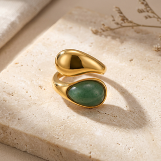 Gold ring with a green gemstone on a textured beige surface