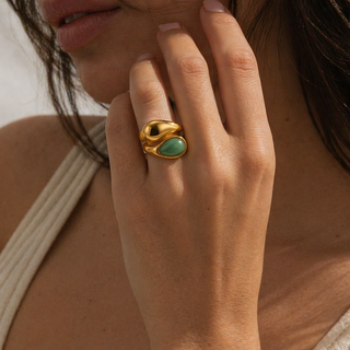 Close-up of a hand wearing a gold ring with a green gemstone.