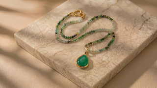 Green beaded necklace with a gold pendant on a marble surface