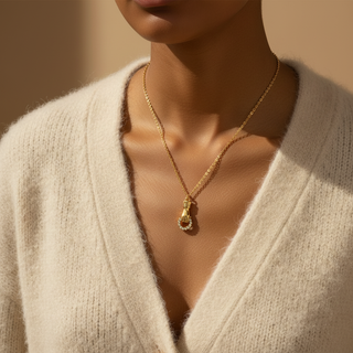 Gold necklace with a pendant worn by a person in a beige sweater.