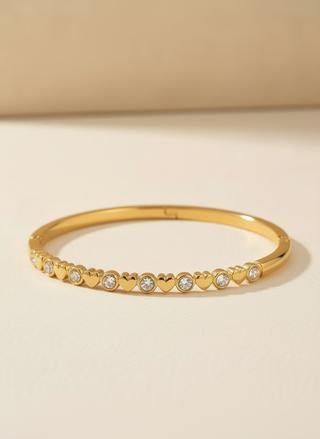 Gold bracelet with heart-shaped cutout and embedded stones on a beige background
