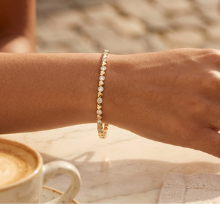 Hand with a bracelet on a table next to a cup of coffee