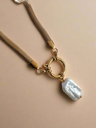 gold plated herringbone chain with a large round clasp and a large freshwater rectangular shaped pearl chain on a white dish