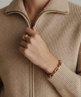 Close-up of a person wearing a beige sweater with a hand adjusting the zipper, wearing a gold ring and bracelet.