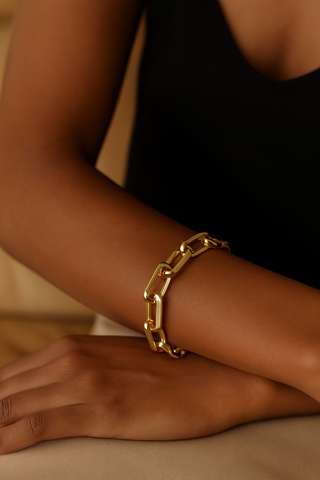 Gold chain bracelet on a wrist with a neutral background