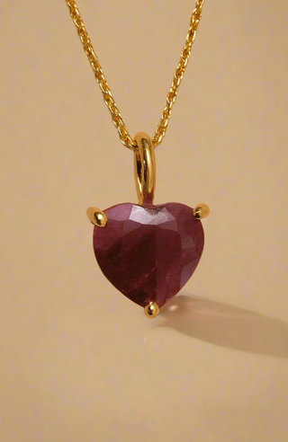 Gold necklace with a heart-shaped purple gemstone on a beige background