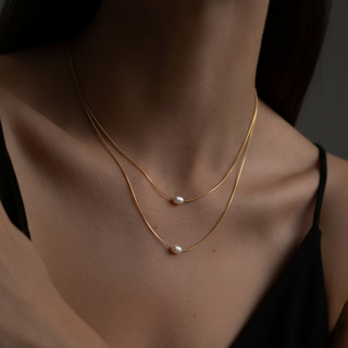 Gold necklace with pearls on a person wearing a black top against a dark background