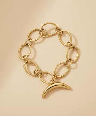 Gold chain bracelet with a crescent moon charm on a beige background