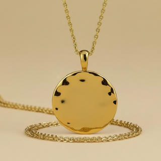 Gold necklace with a round pendant on a beige background