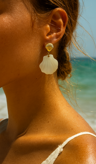 Close-up of a person wearing shell earrings with a beach background